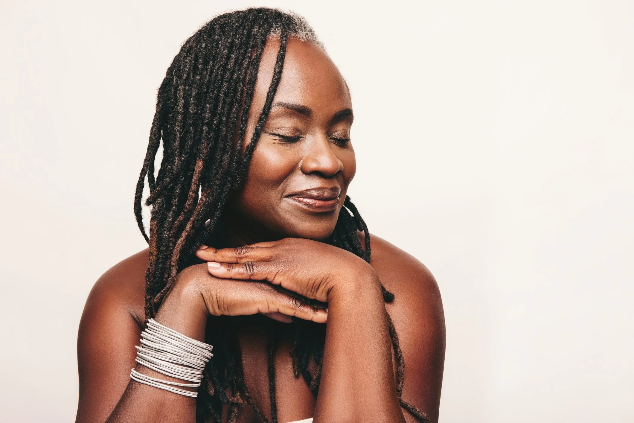 Woman with long locs and glowing skin smiling peacefully against a light background