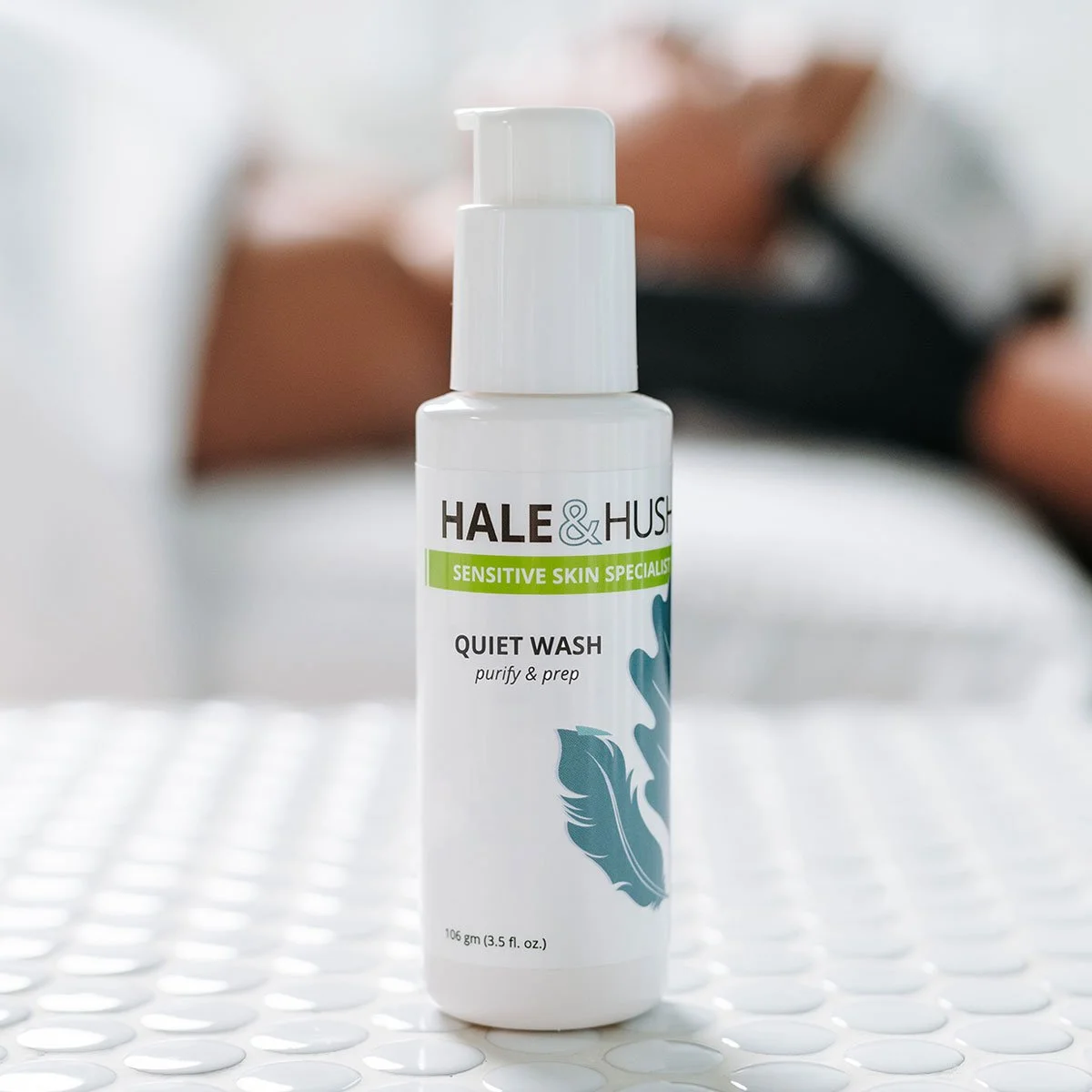 A white bottle of Hale & Hush Quiet Wash on a white textured surface with a blurred background