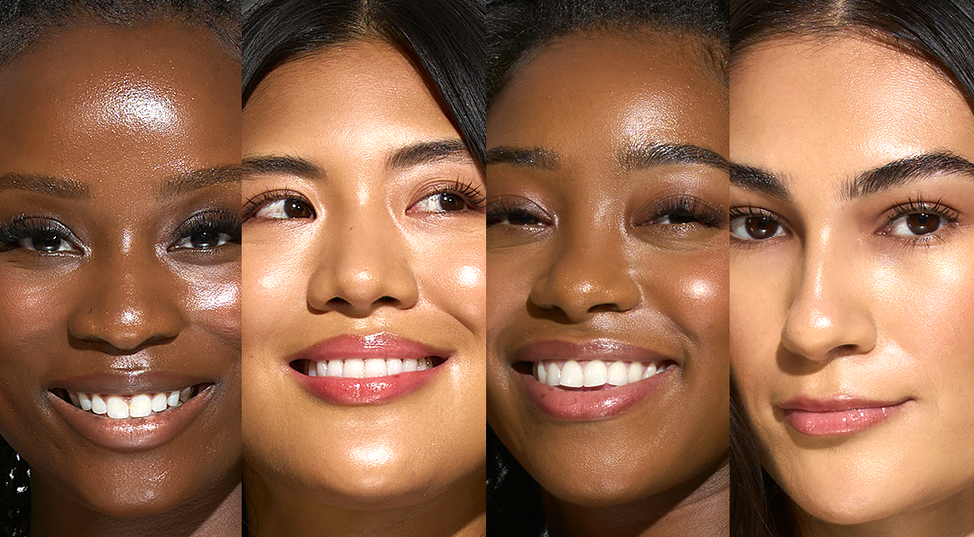 Close-up of four women with diverse skin tones and hairstyles, smiling and looking at the camera.