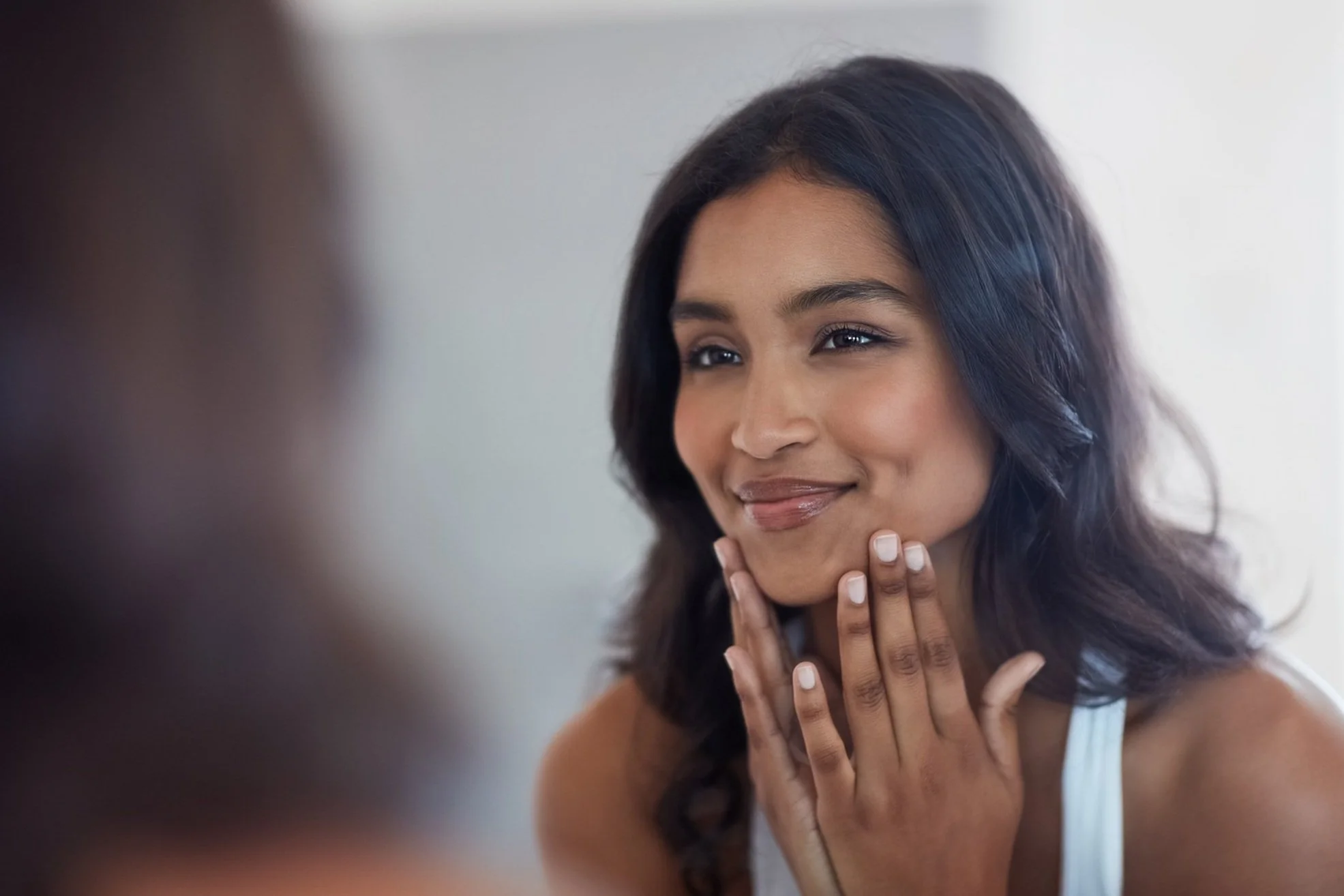 Woman with healthy-looking skin and natural makeup smiling before a skincare treatment
 with her hands on her chin.