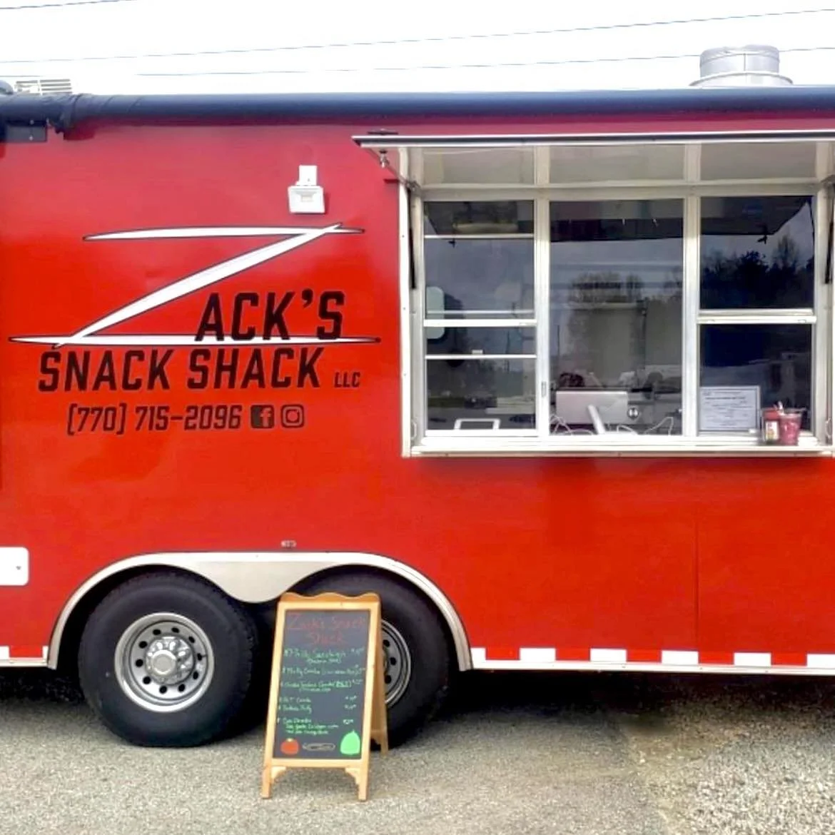 A red food truck named Jack's Snack Shack LLC with a window for ordering, and a small chalkboard menu on an easel outside.
