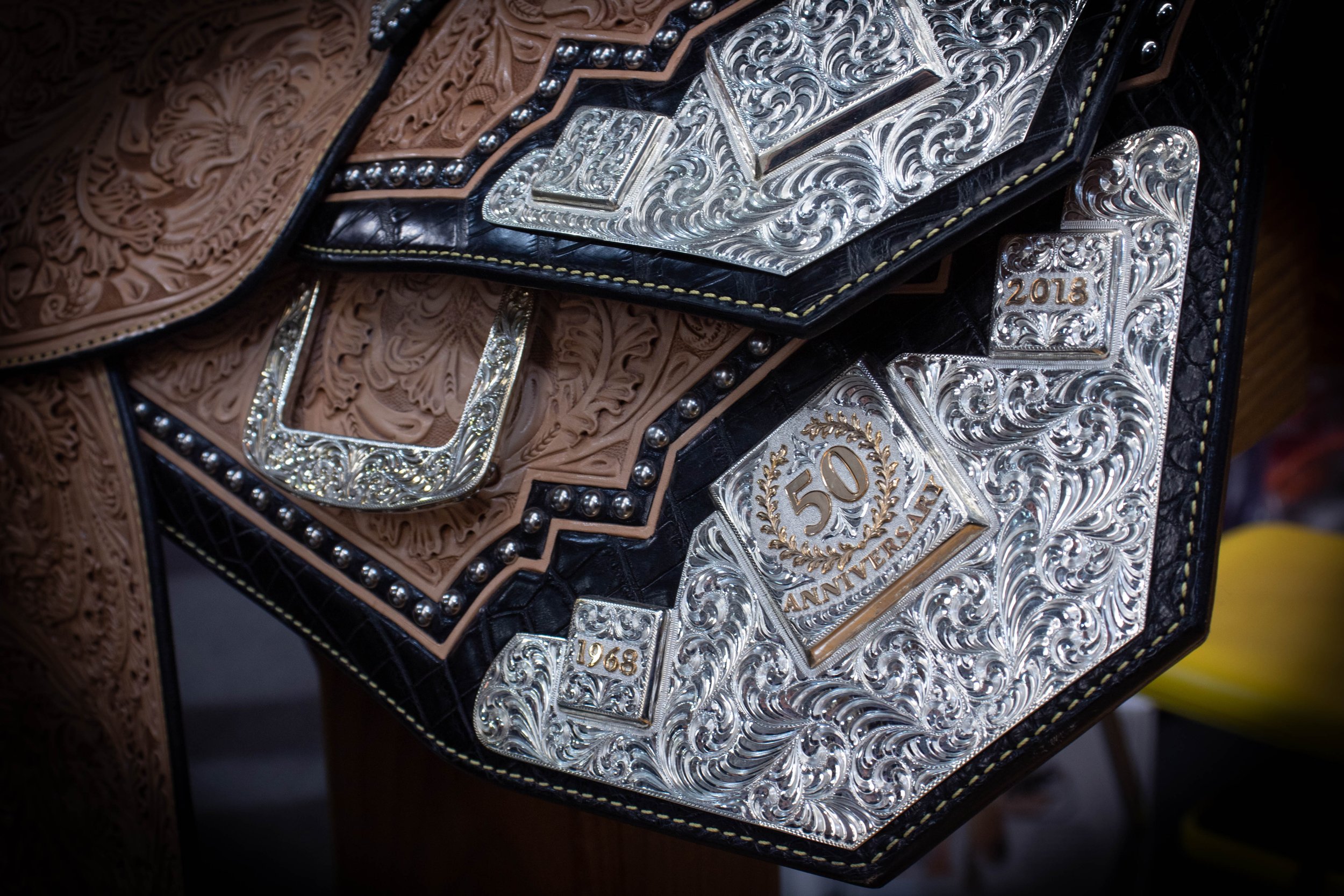 A close-up of a wrestling championship belt with intricate silver and gold designs, including the years 1963 and 2018, and decorative patterns.