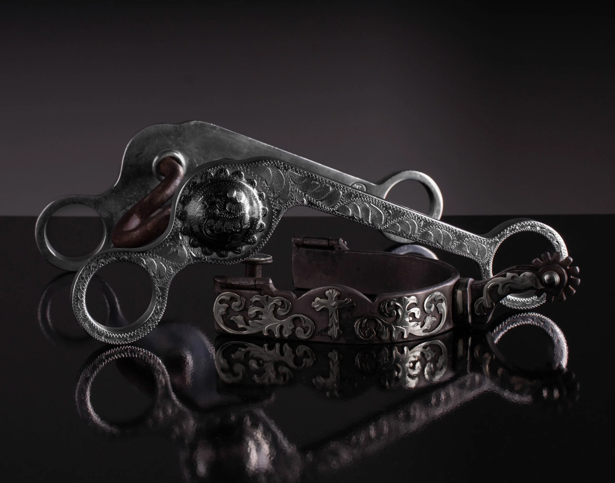 Decorative silver guns with intricate engravings and dark wooden grips, laying on a reflective black surface.