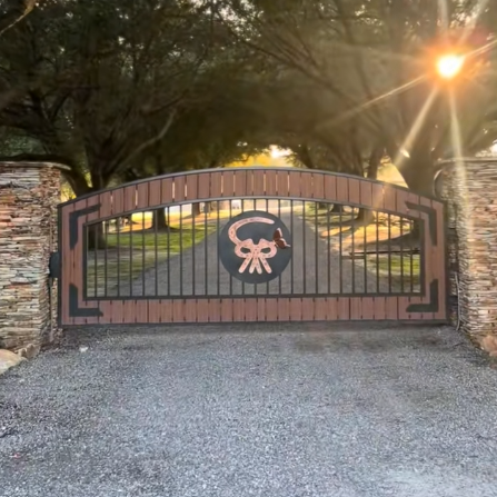 Iron gate with skull emblem, flanked by brick pillars, leading into a scenic landscape with trees and a sunset.