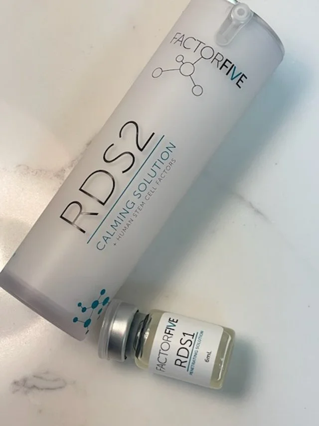 A white cylindrical container labeled FACTORFIVE RDS2 Calming Solution and a small glass vial labeled FACTORFIVE RDS1 on a white marble surface.