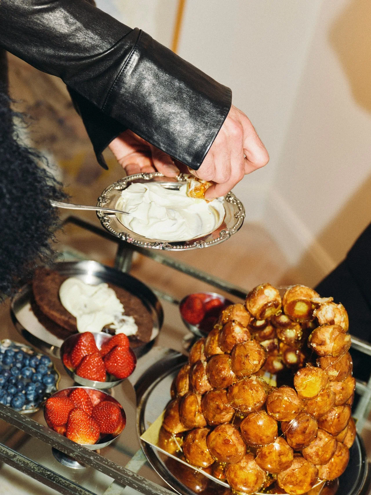 Hands gathering around an abundant edible table with fruit, cheese and pastries at a Feast with Fiore event in Los Angeles.