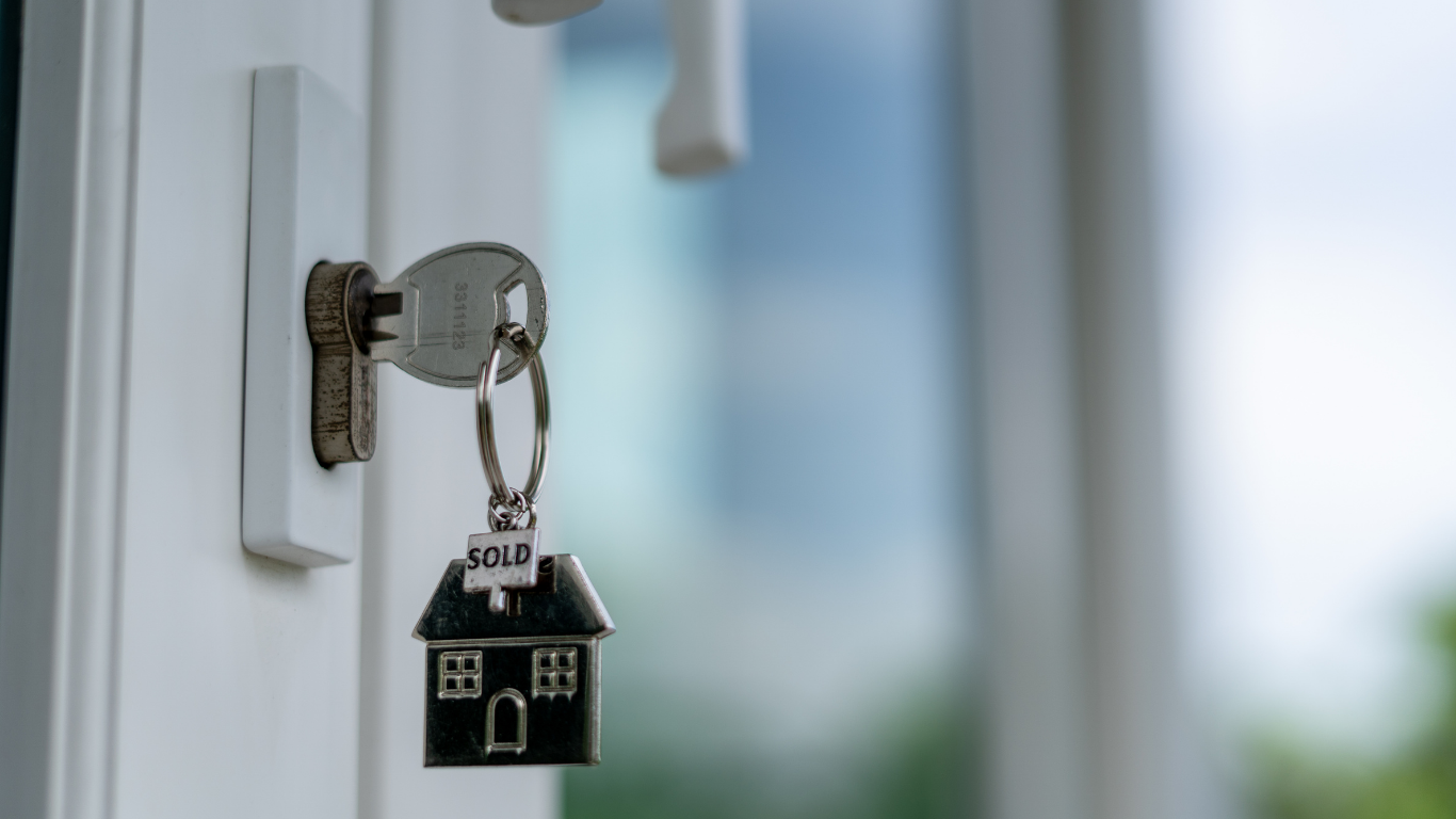 Key with house-shaped keychain marked 'sold' hanging in a door lock.