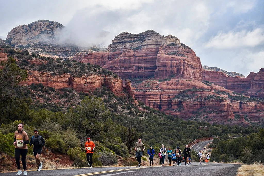 runners on half marathon course that is set on the road. The iconic red rocks of sedona are in the background with clouds.