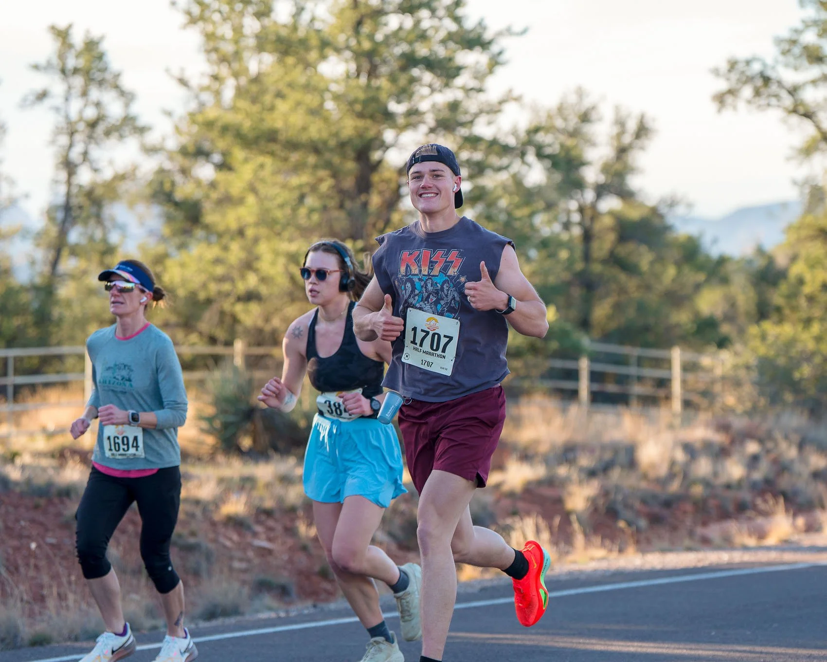Young man with a band t-shirt and backwards hat running with two thumbs up in RunSedona Half Marathon