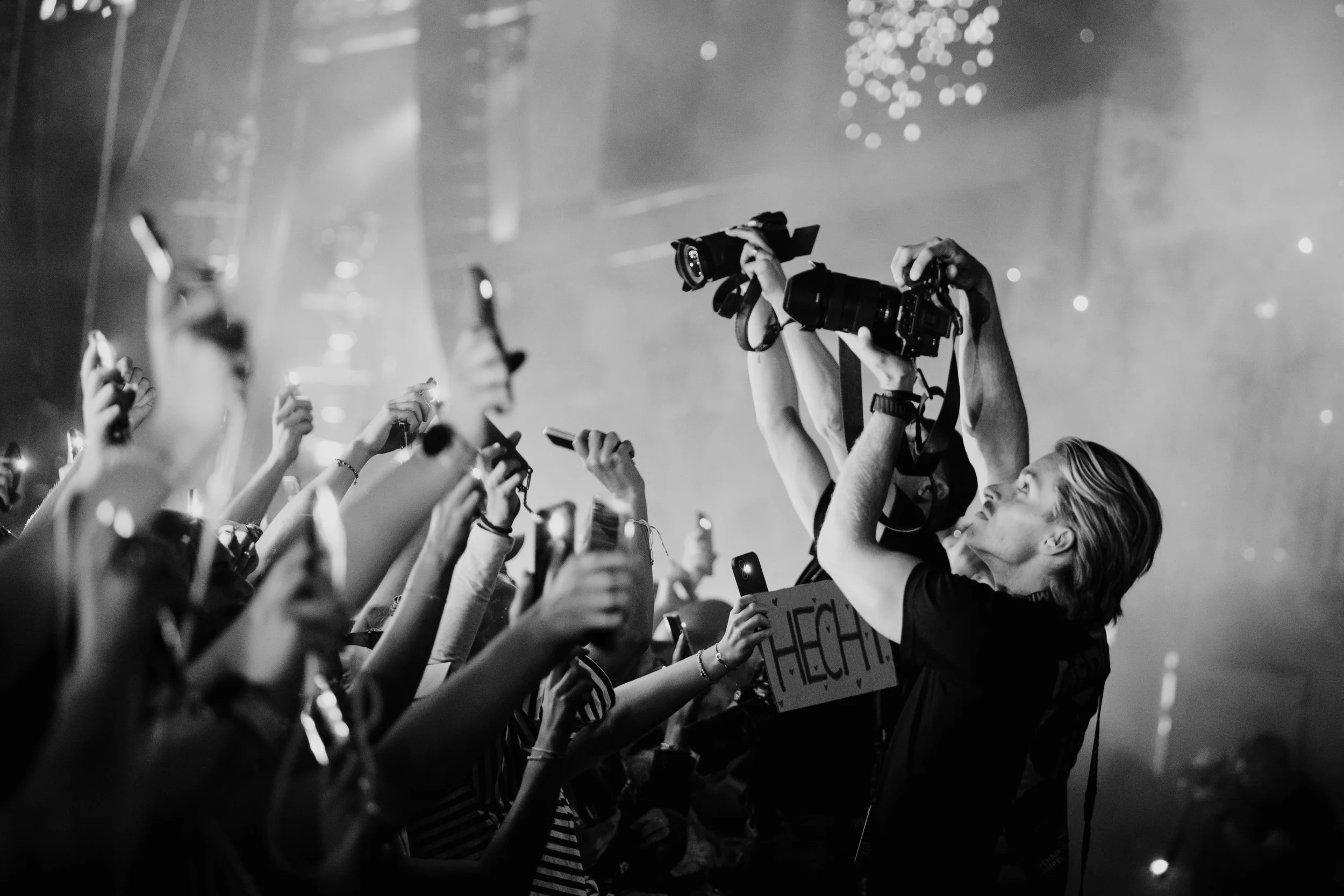 Menschen bei einem Konzert, die Kamera und Smartphones in der Hand halten, in einer dunklen, festlichen Atmosphäre.