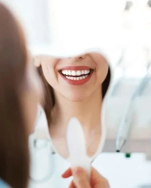 Una donna si guarda allo specchio sorridente mentre si prende cura del sorriso.