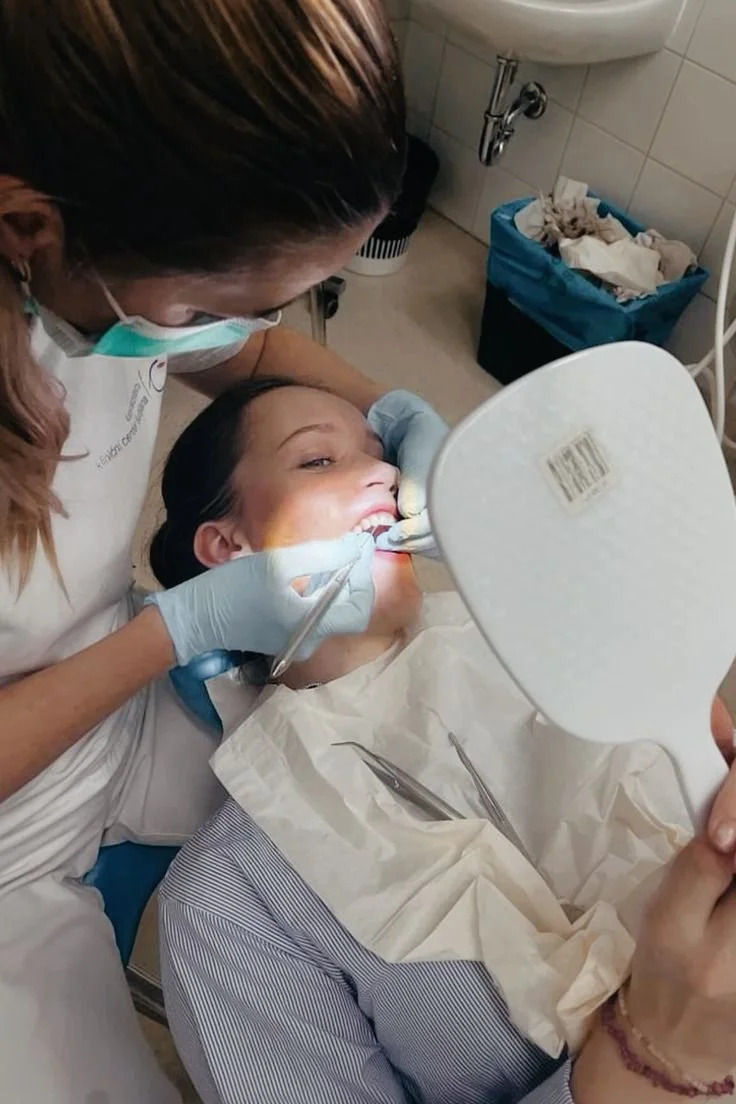 Una donna sta sottoponendosi a un trattamento dentistico mentre una professionista le fa una pulizia dentale in un ambulatorio.