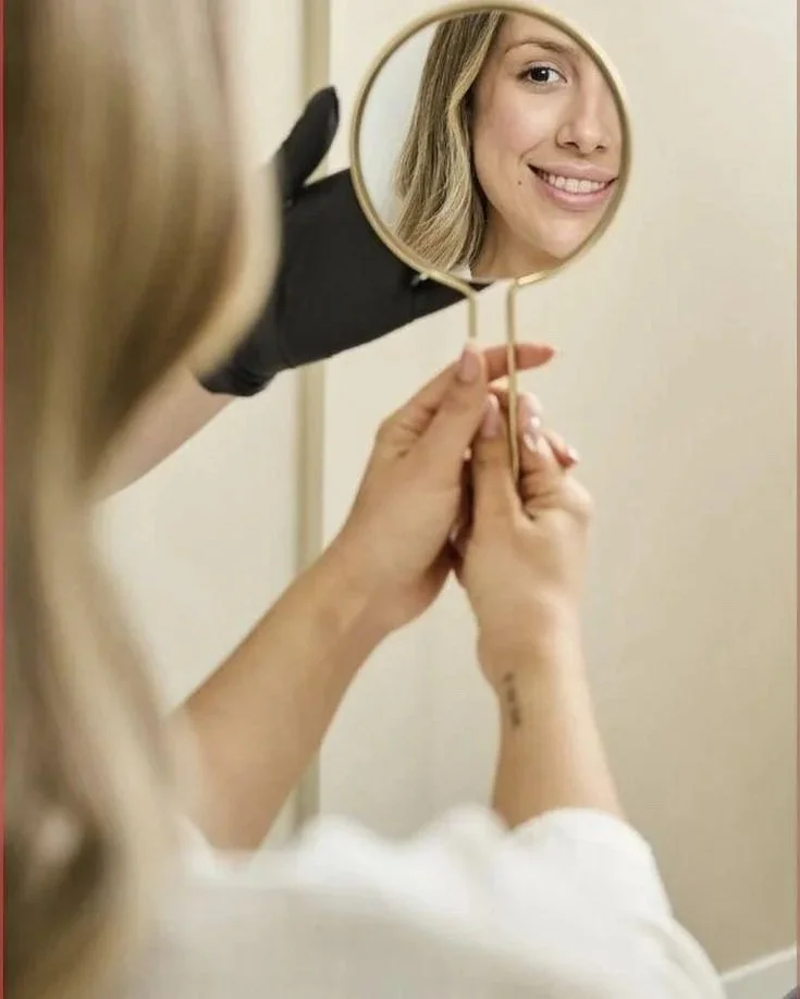 Una donna si sta guardando nello specchio e sorride, riflessa in un piccolo specchio rotondo.