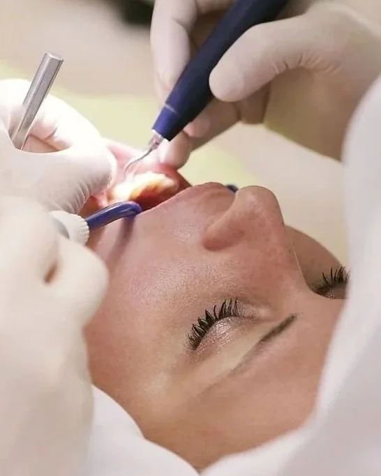 Dentista che esegue un trattamento odontoiatrico su un paziente disteso, con strumenti dentali in uso.