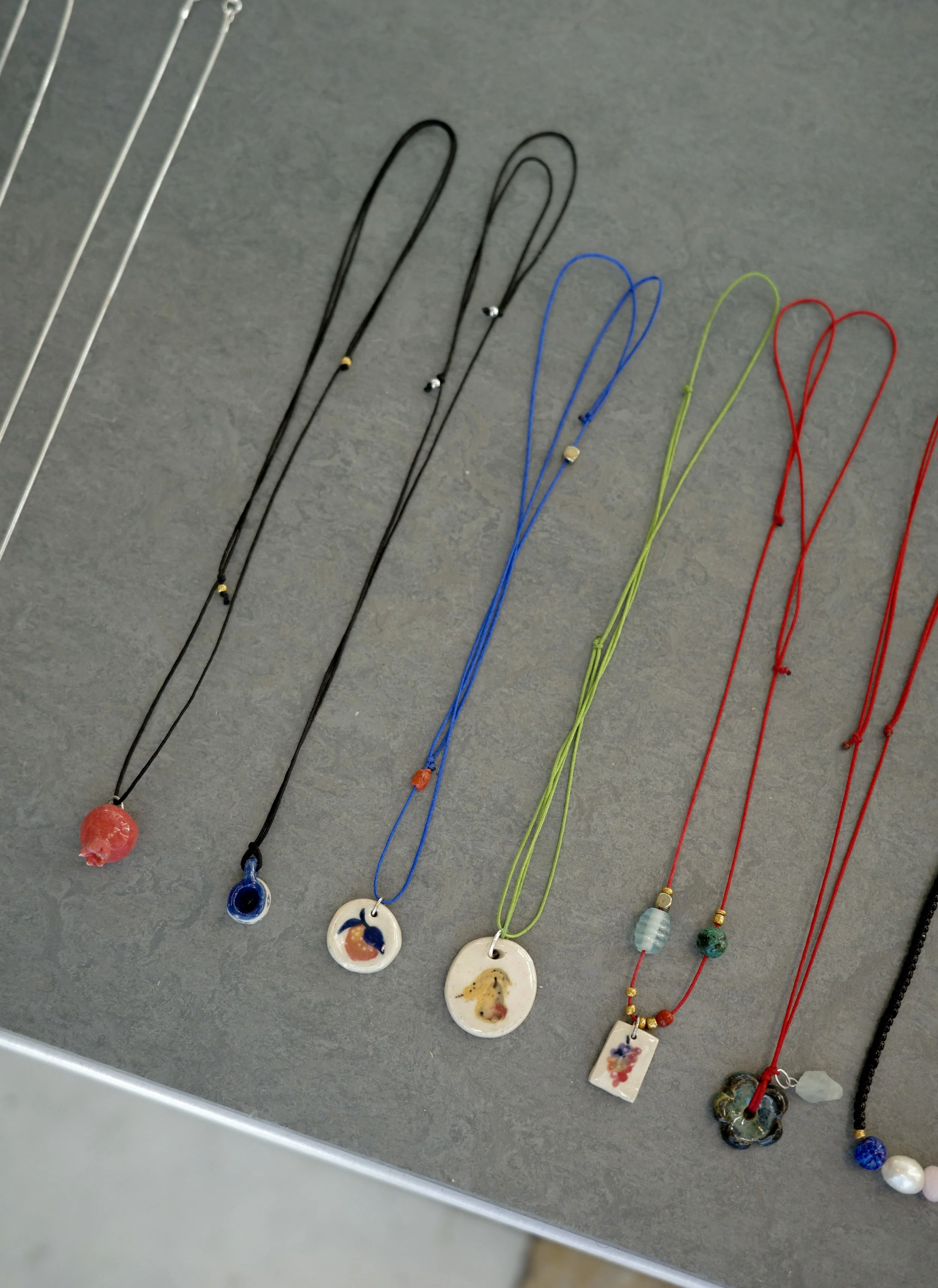 Colorful necklaces with pendants featuring small animal and nature designs, displayed on a gray surface.