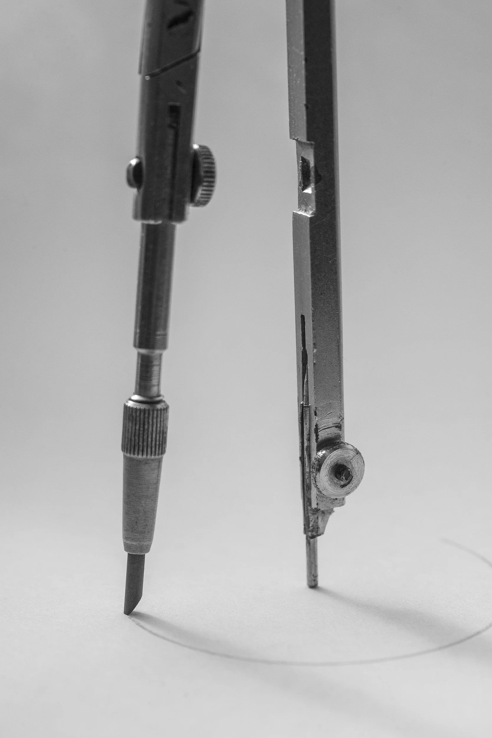 A close-up of a precision drawing compass drawing a circle on paper.