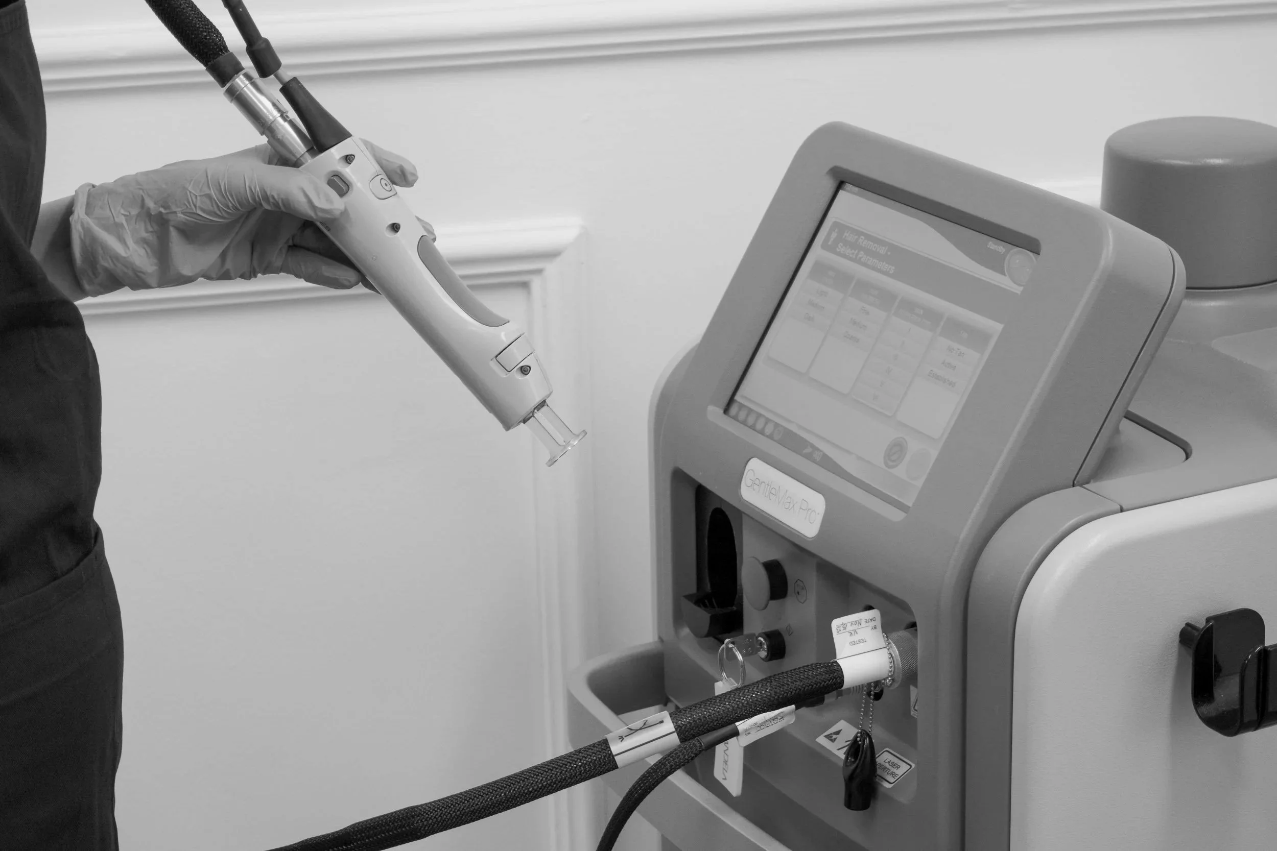 A medical professional wearing gloves using a handheld device attached to a machine labeled "GentleMax Pro" in a clinical setting.