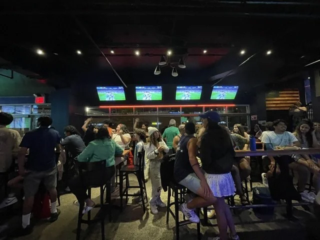 Crowded sports bar with people watching multiple TV screens showing a sports game.