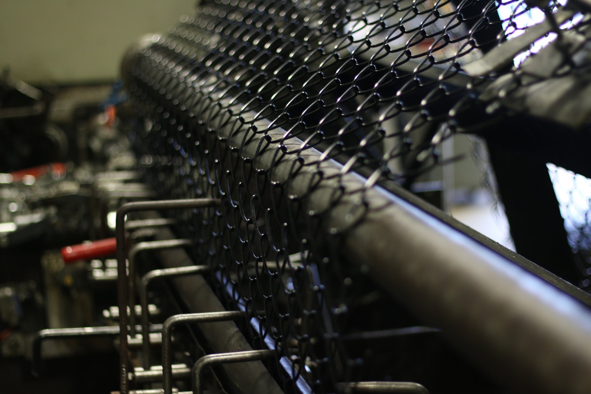 Close-up of a chain-link fence weaving machine making black vinyl coated chain-link fence fabric.