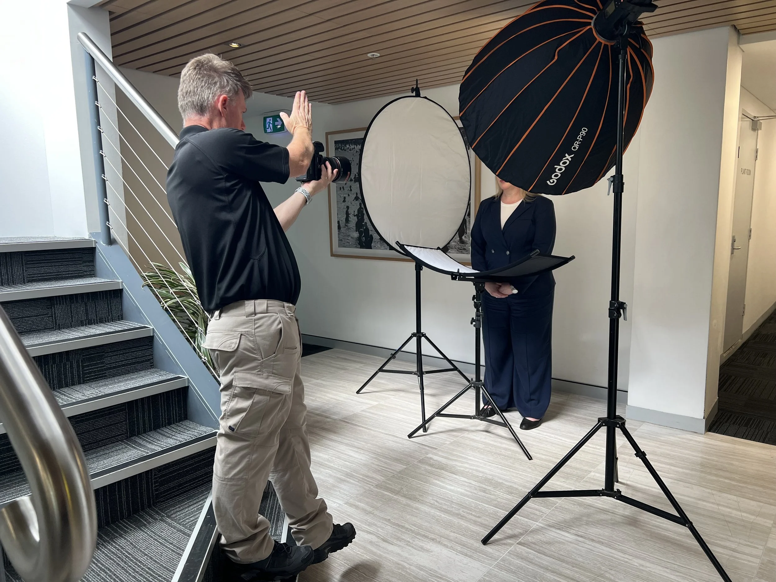 A photographer is taking a picture of a woman during a photo shoot indoors with professional lighting equipment.