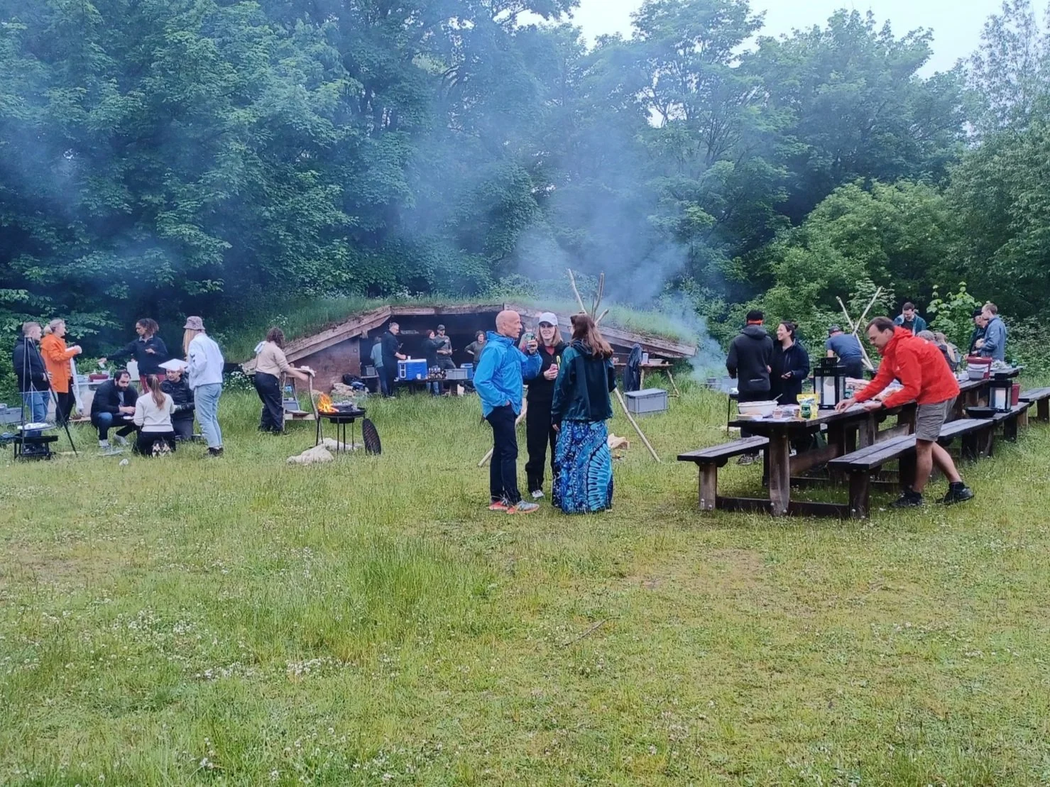 En gruppe mennesker er fuld gang med at snakke, dække bord og tilberede mad over bål