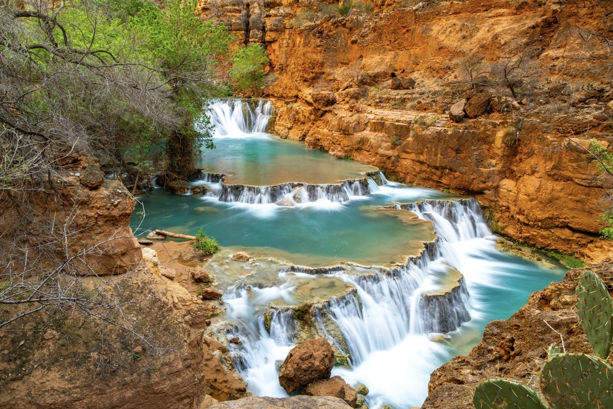 Scenic view of Beaver Falls cascading into a turquoise pool surrounded by red rock canyon walls in Havasupai, Arizona.
