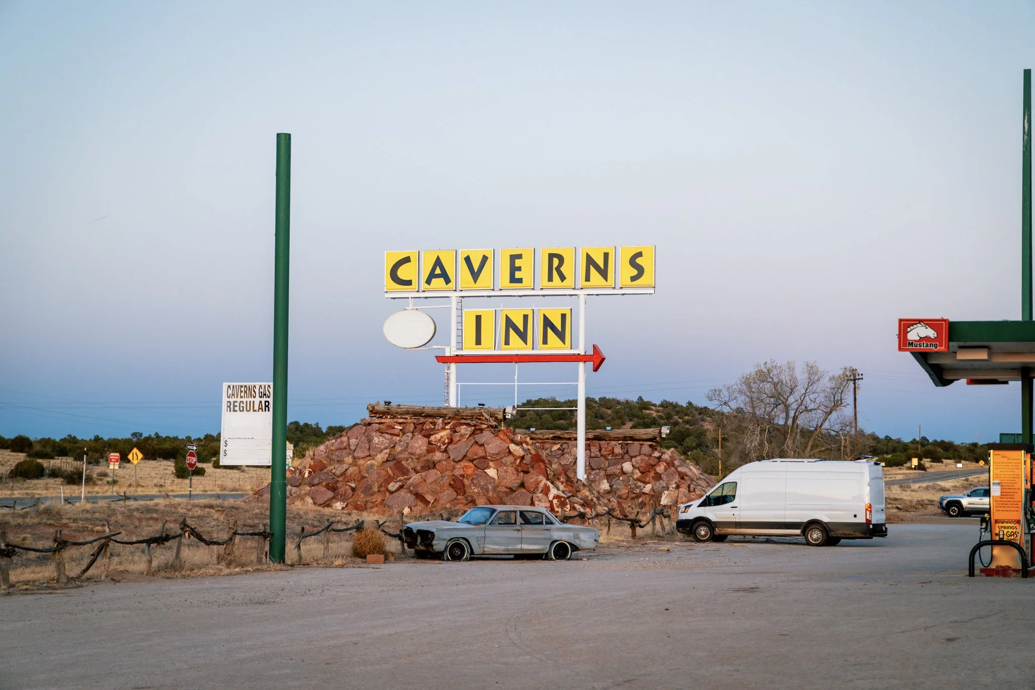 Vintage Caverns Inn sign next to gas station at sunset, with an old car and service van parked nearby along Route 66 in Arizona