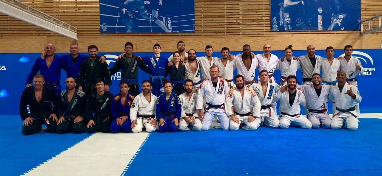 Group of people wearing martial arts uniforms in a gym with blue mats, posing for a photo.