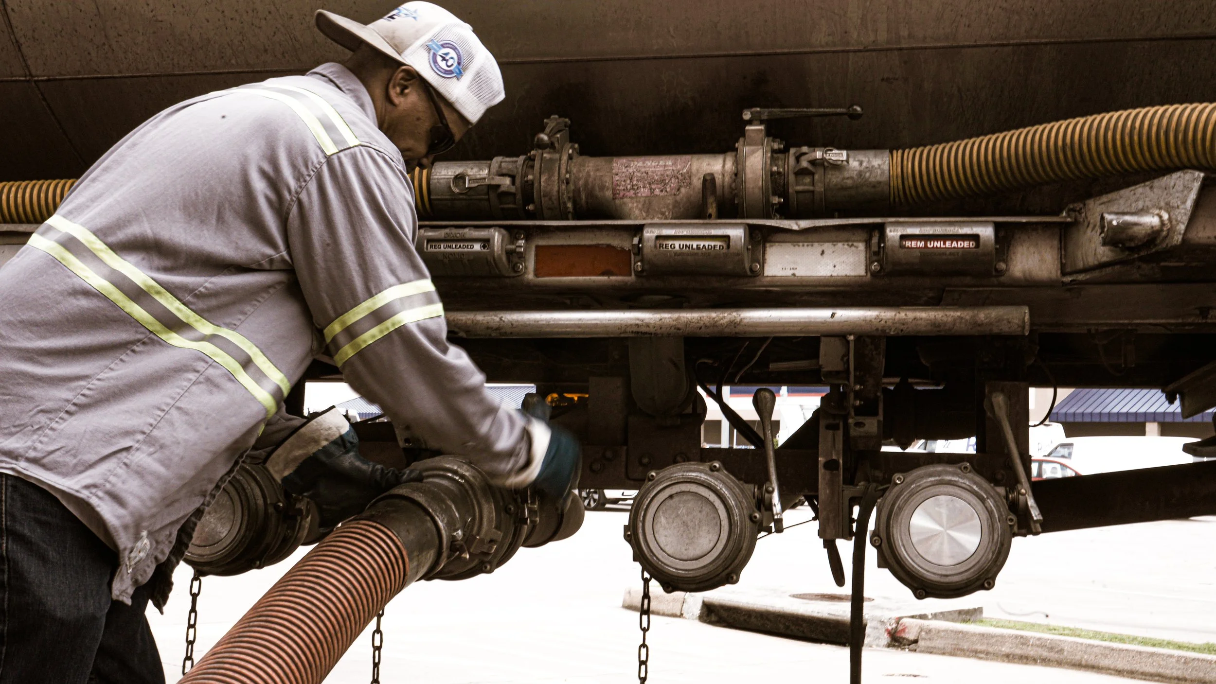 Worker inspecting or repairing large industrial vehicle or equipment with hoses and machinery underneath.