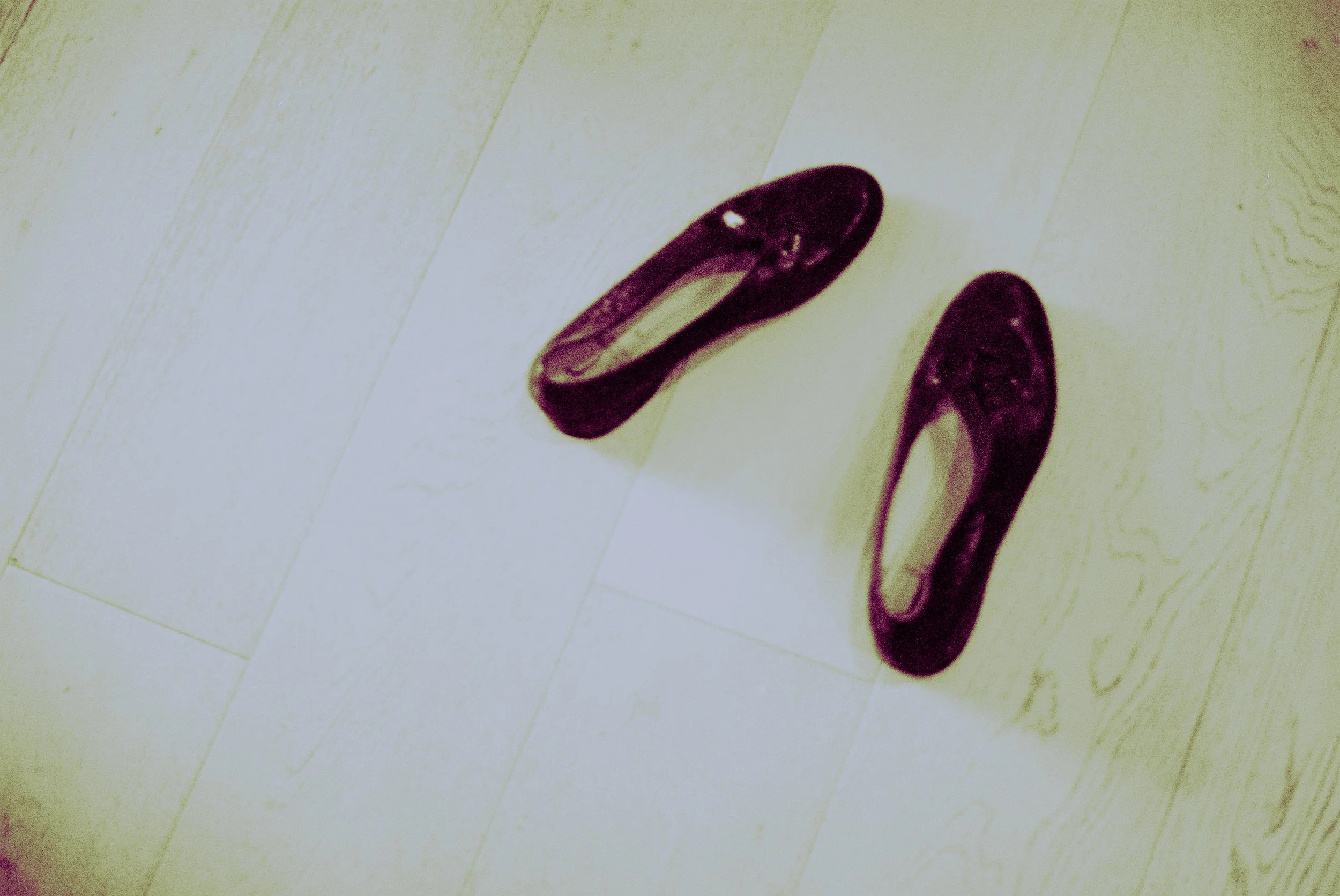 A pair of purple high-heeled shoes lying on a light-colored wooden floor.
