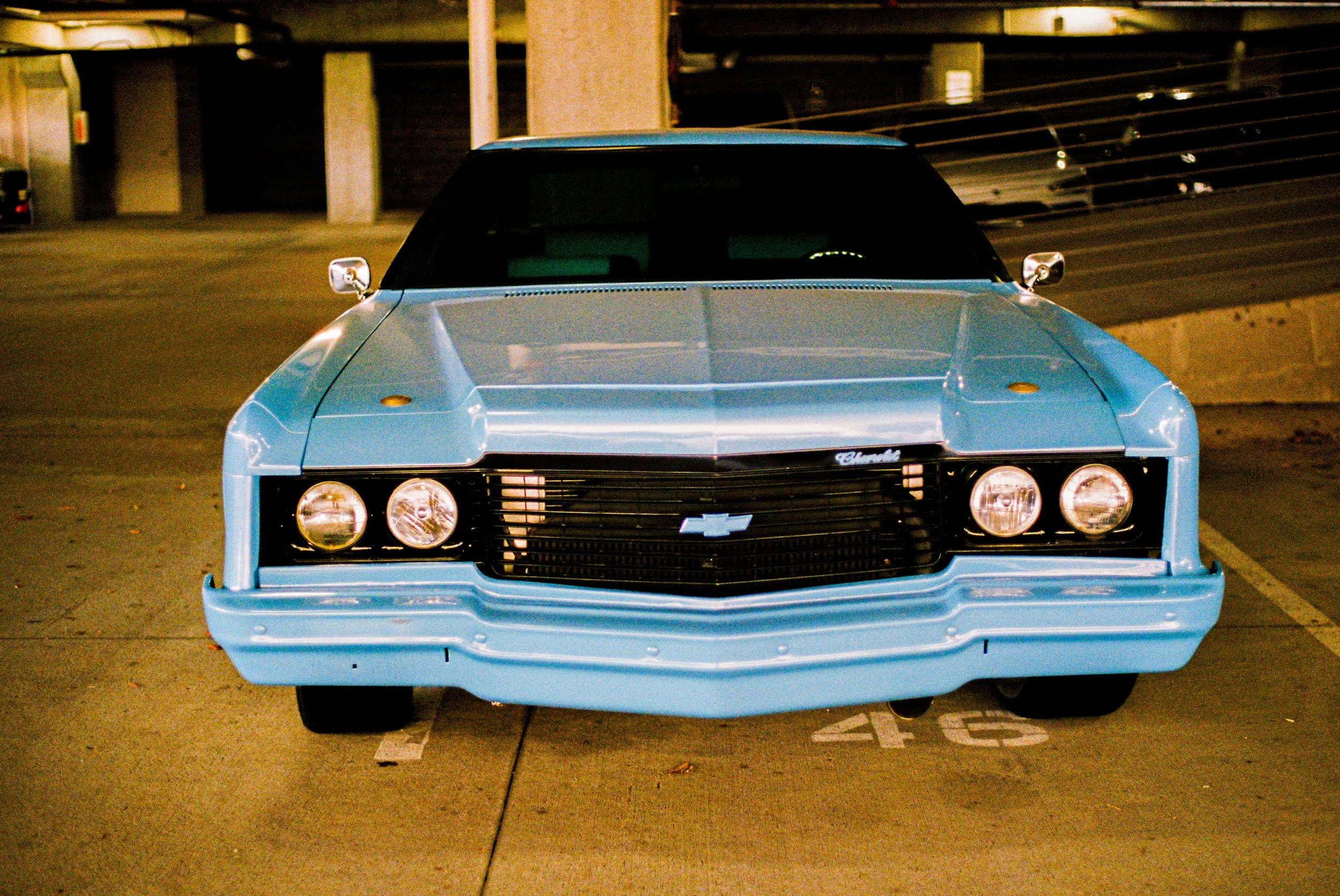 Front view of a vintage light blue Chevrolet Camaro parked in an underground parking garage.