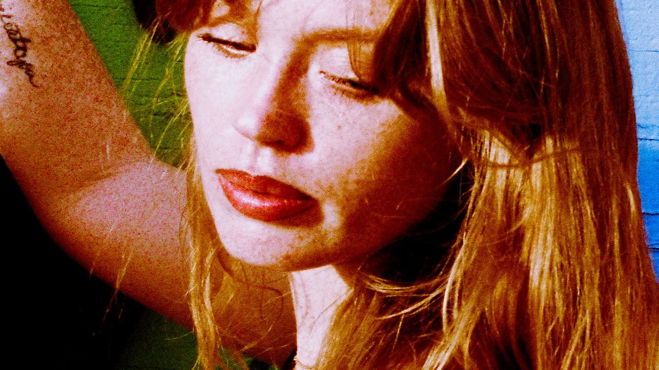 Close-up of a woman with red hair and closed eyes, lying on a green and blue surface.