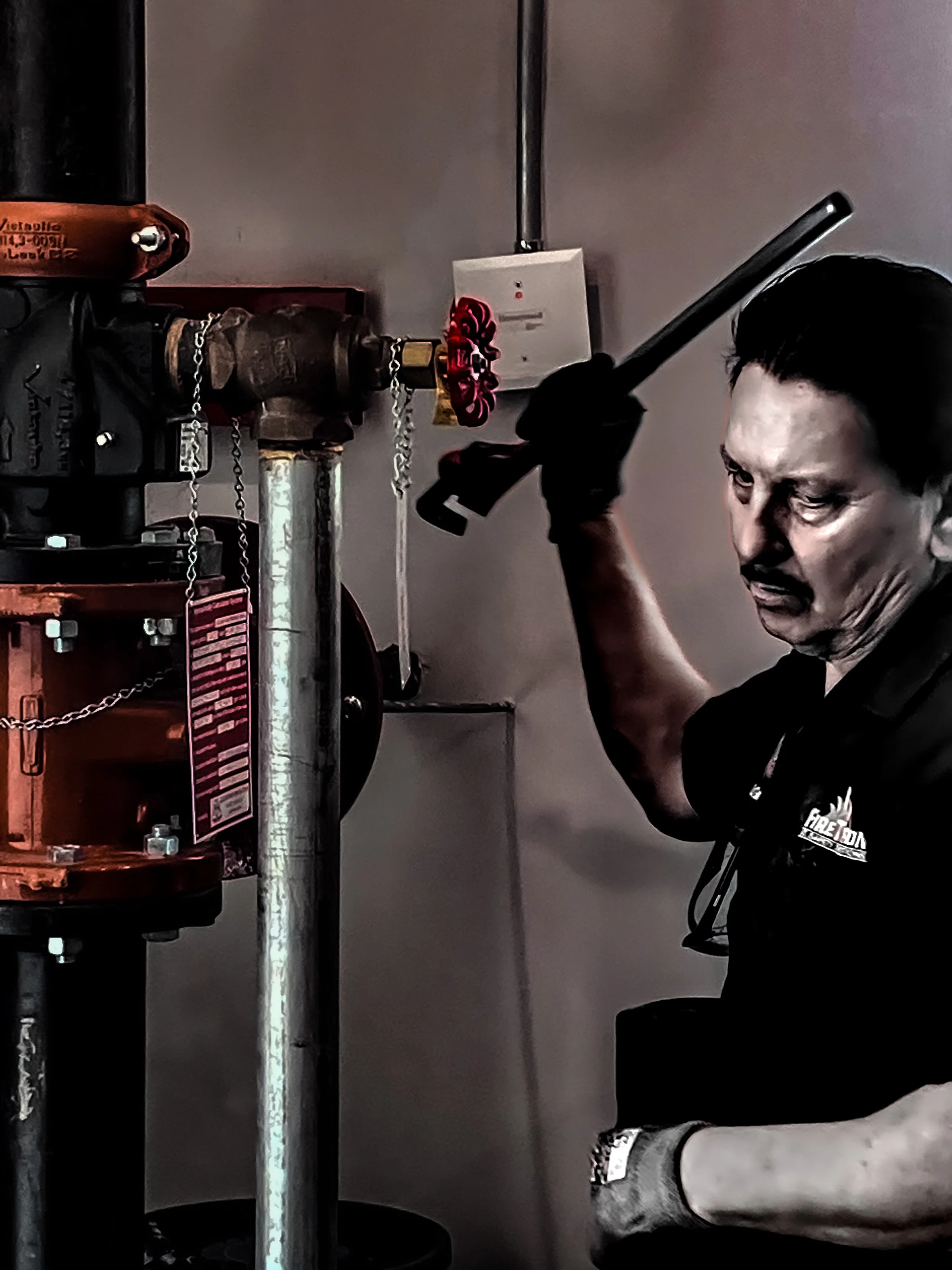 A firefighter using a pipe wrench to operate a valve on fire suppression equipment.