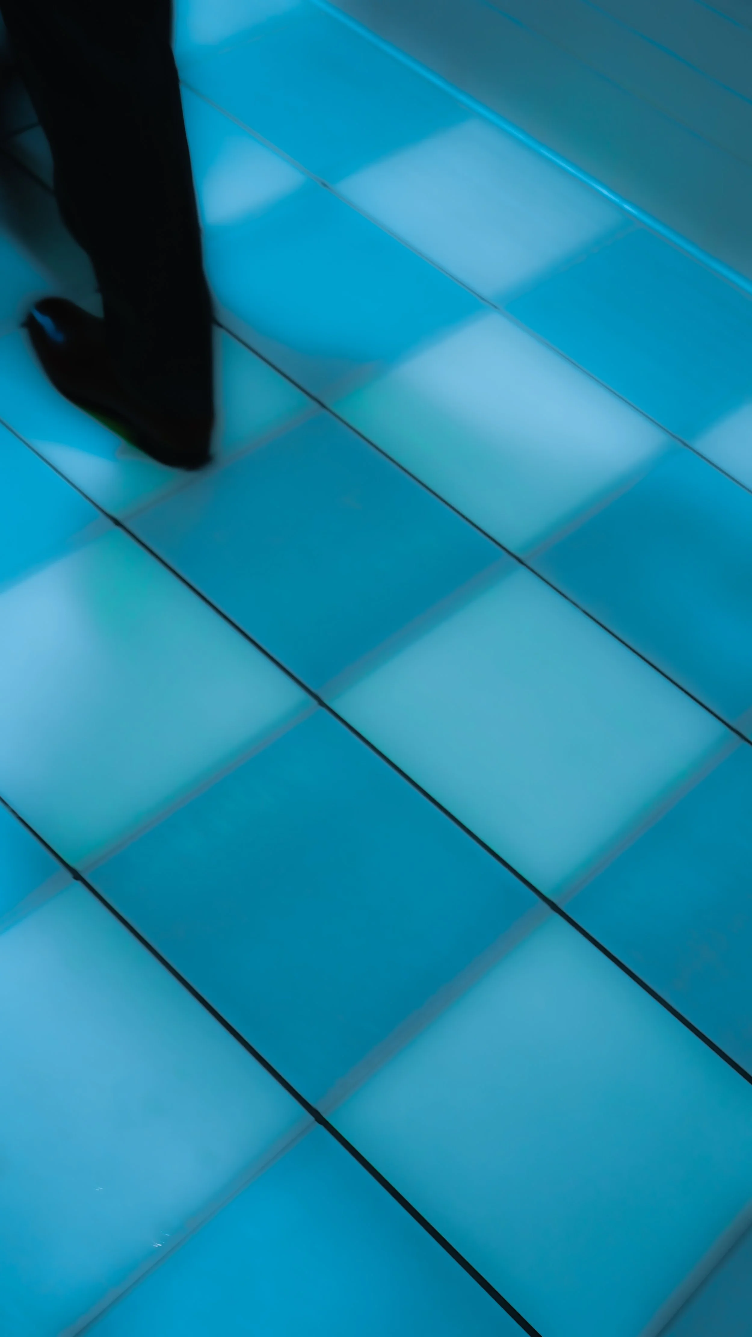 Part of a person’s legs and feet standing on illuminated blue floor tiles.