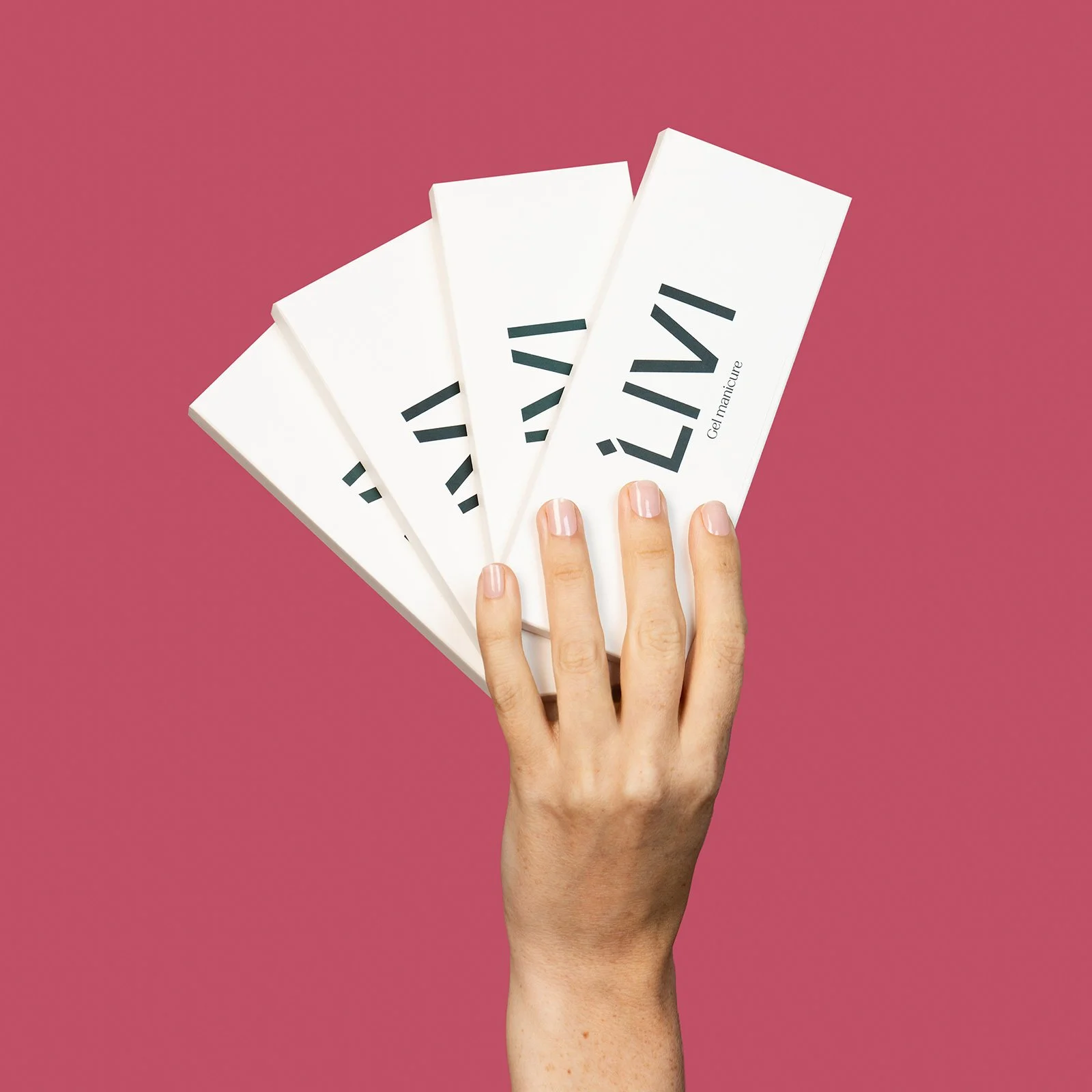 A hand with manicured nails holds four white boxes labeled "LIVI" against a pink background. The image conveys elegance and minimalism.