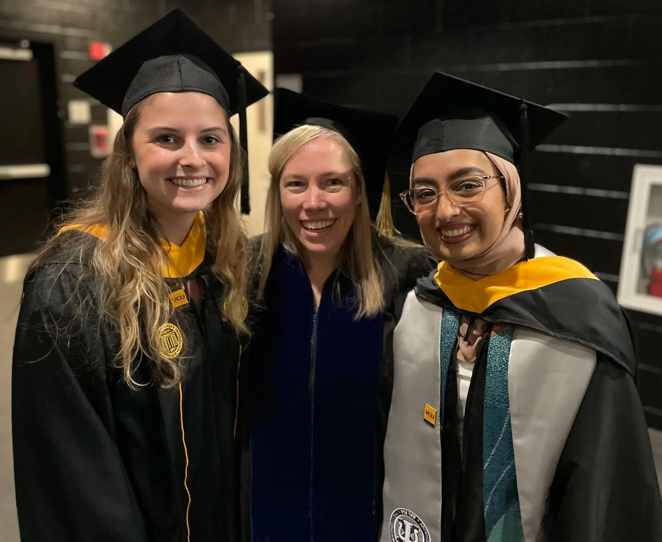 Three women in graduation caps and gowns taking a selfie together.