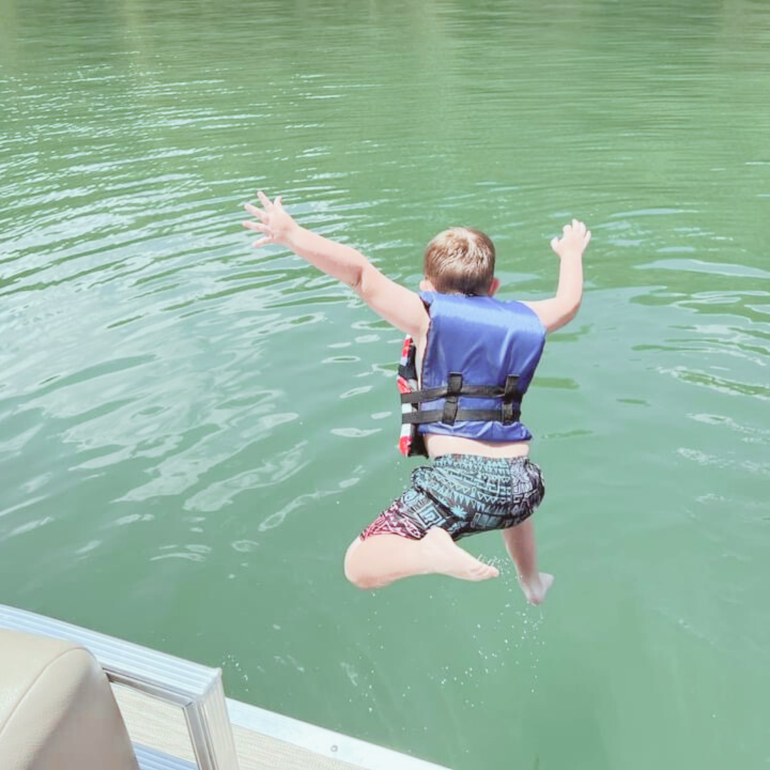 Child jumping into a body of water wearing a life jacket and swimming trunks.