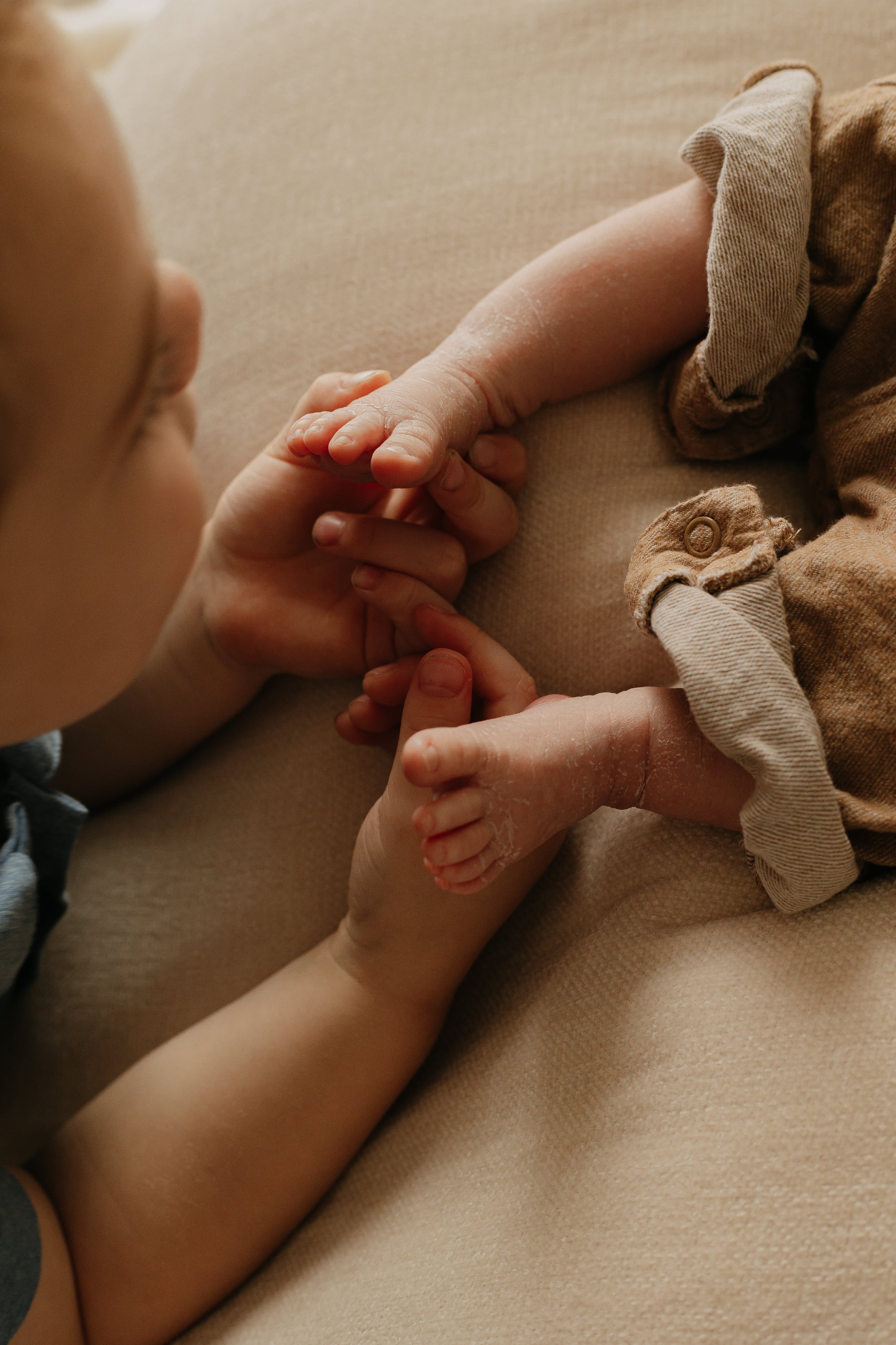 A young child holding baby's feet, with the child's face partially visible and the baby's legs and feet in focus.