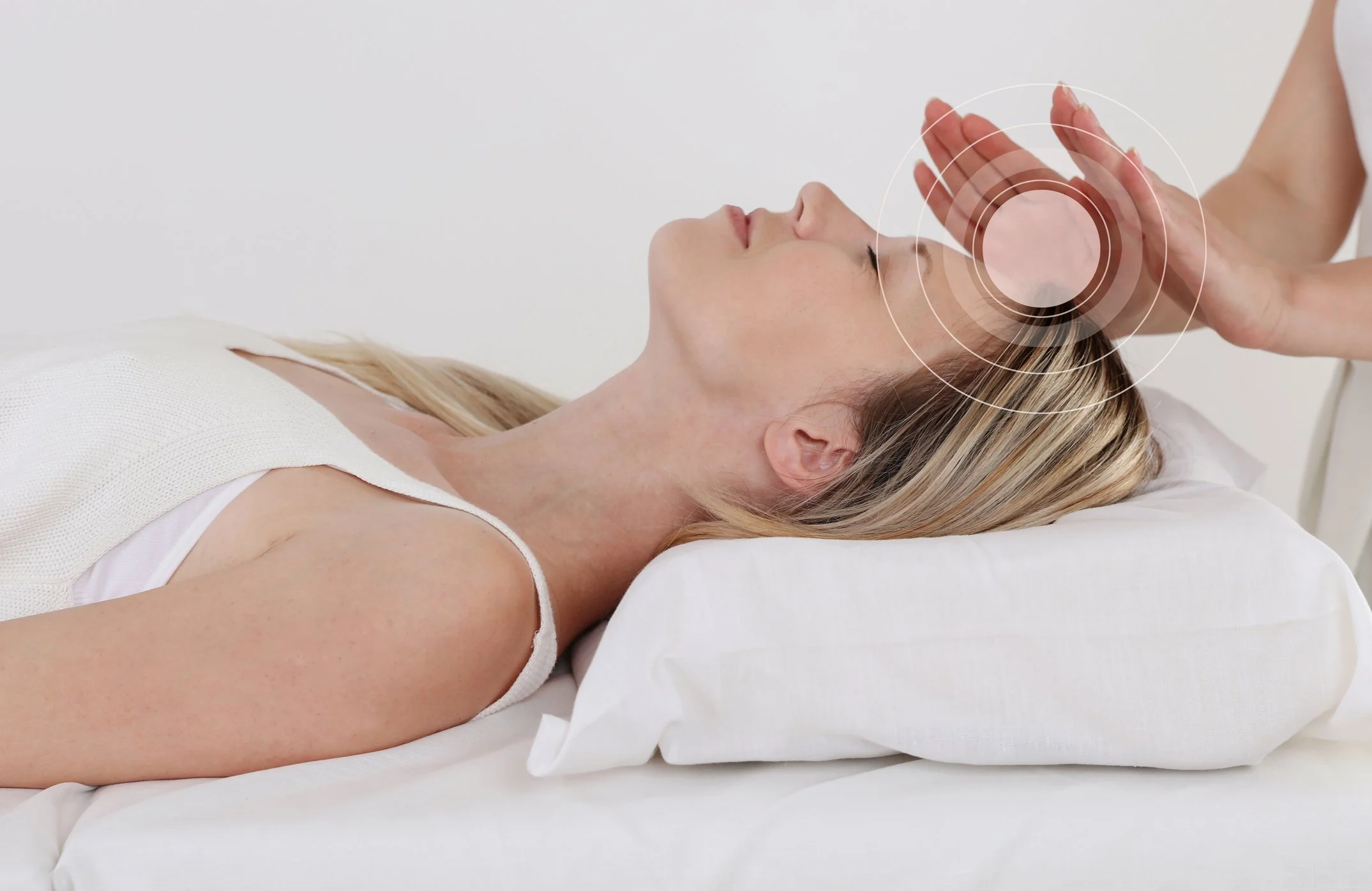 A woman lying on her back on a bed, receiving a cranial massage or therapy from a practitioner, with a circular digital overlay near her forehead.