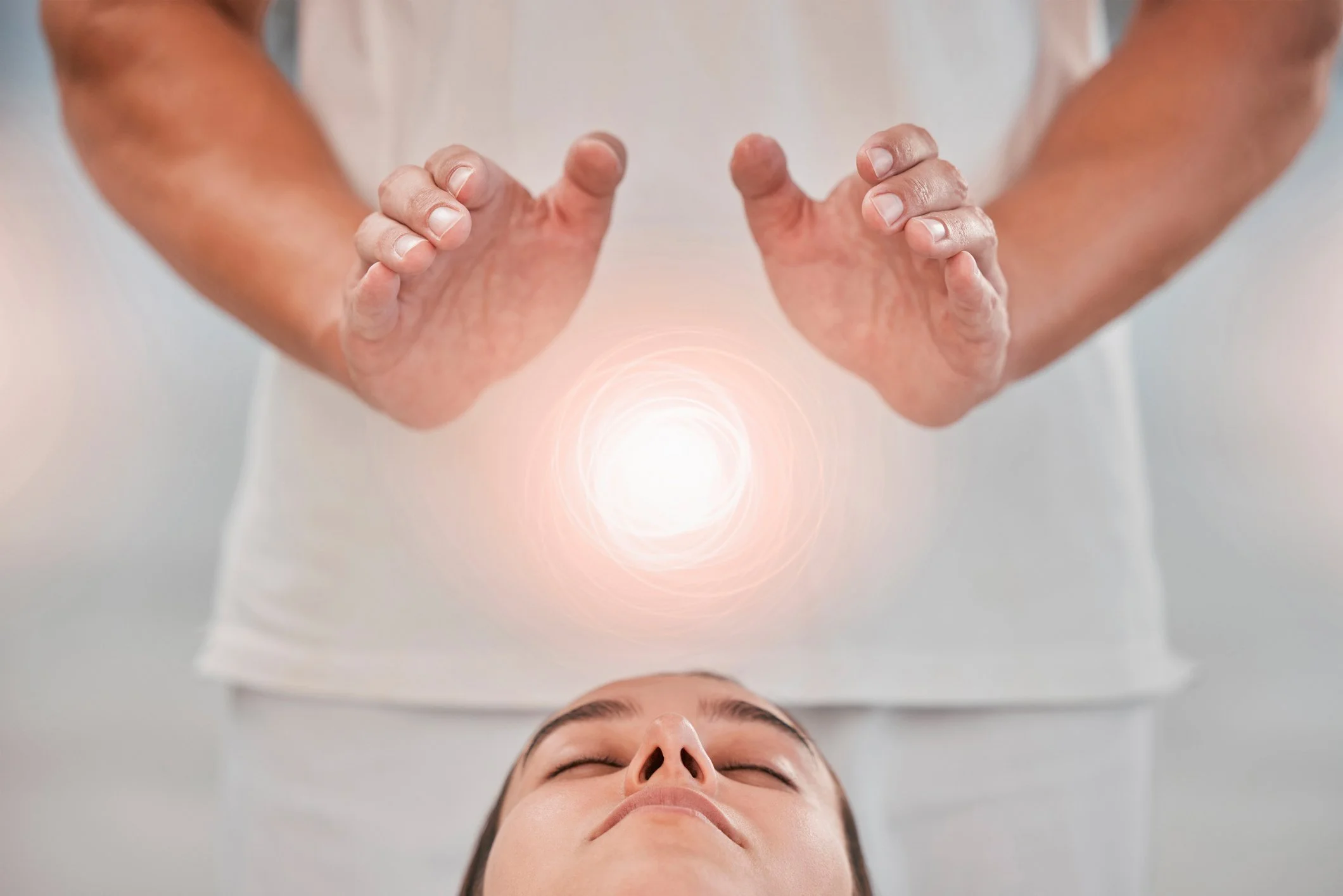 A person lying down with their eyes closed, while another person hovers their hands above the person's chest with a glowing light in between.