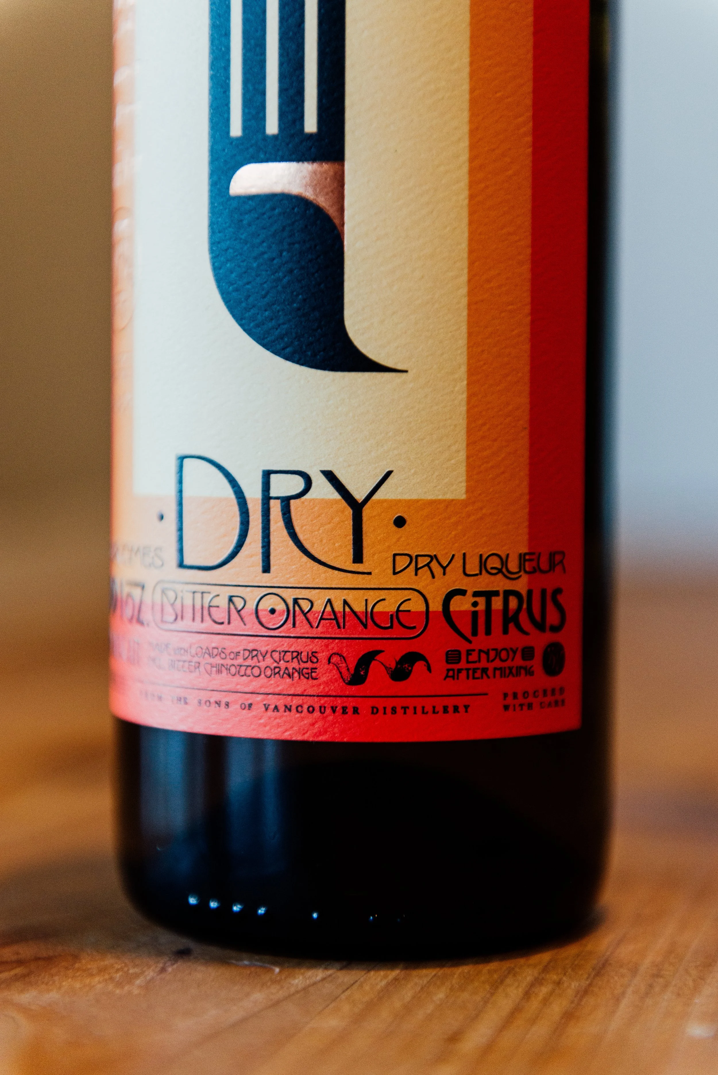 Close-up of a bottle of dry citrus liqueur with a colorful label featuring orange and yellow stripes and black text.