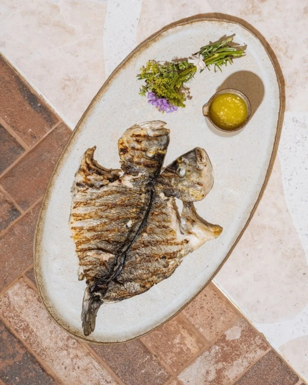 Olon Ps&aacute;ri /ὅ&lambda;&omicron;&nu; &psi;ά&rho;&iota;/ (n.) &mdash; whole fish

The heart of Aegean cooking, where simplicity meets the sea.
Sourced fresh and grilled over flame, brushed with orange blossom honey and ladolemono, and finished wi