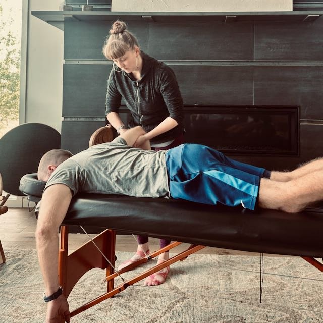 woman stretching a man on a massage table outside, surrounded by bicycles and people sitting in chairs
