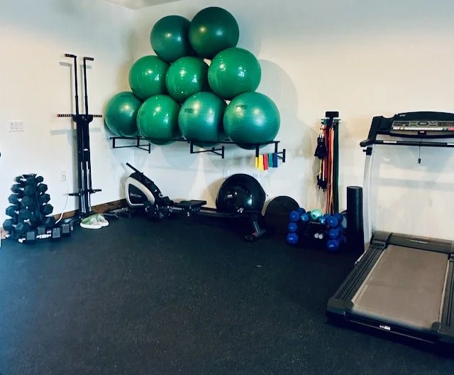 Studio gym with green exercise/swiss balls on wall-mounted shelves, a treadmill, dumbbells, kettlebells, resistance bands, a vertical climber, and a row machine.