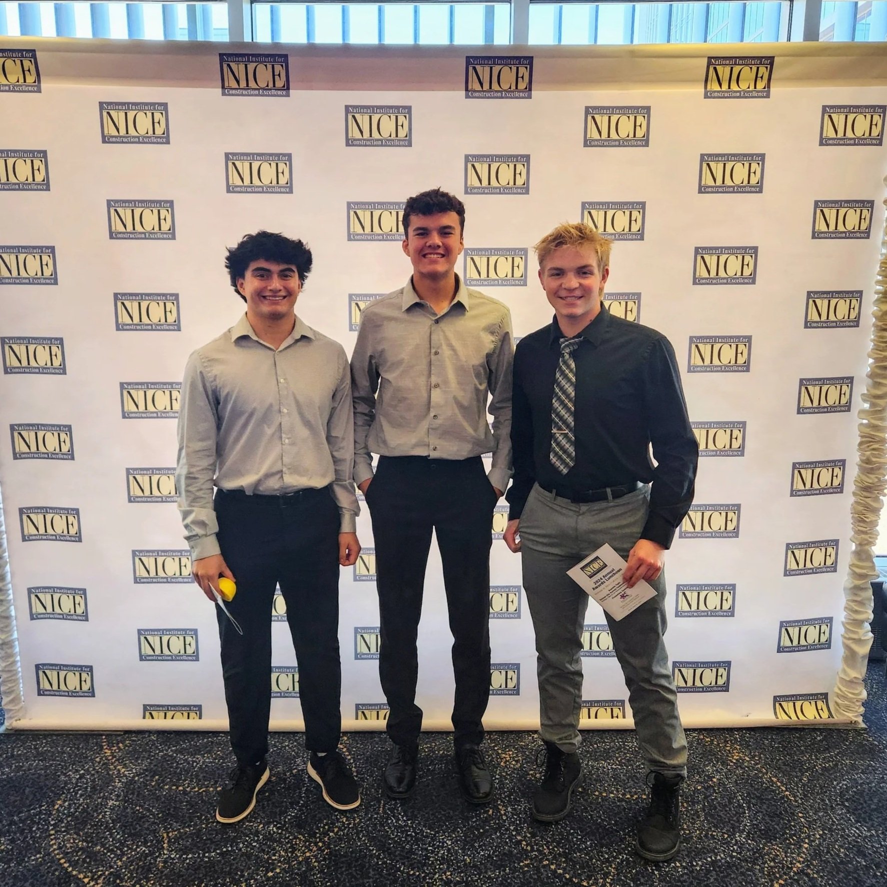 Three students pose in front of a conference photo backdrop during a professional event.