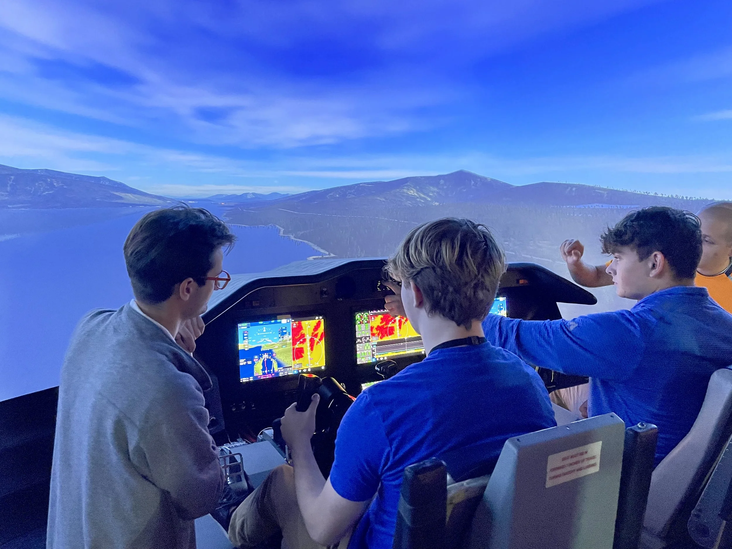 A group of Northland CAPS students working in a flight simulator with instrument panels and navigation screens while receiving instruction.