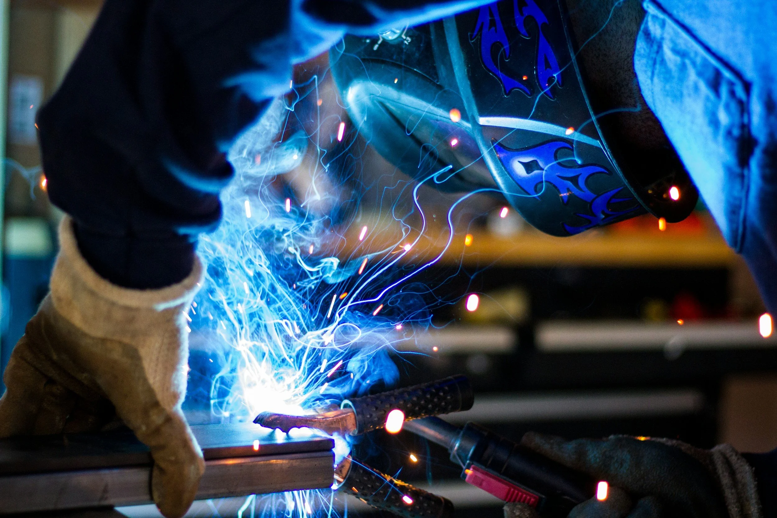 A person welding metal with sparks and bright blue light in a workshop.