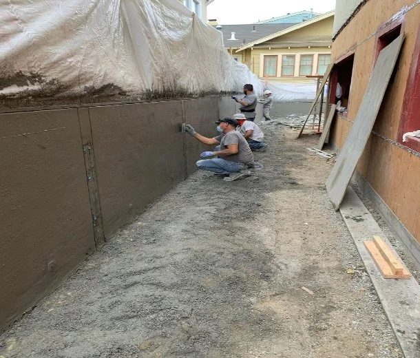 Construction workers applying a layer of stucco or cement to the exterior wall of a building during construction or renovation.