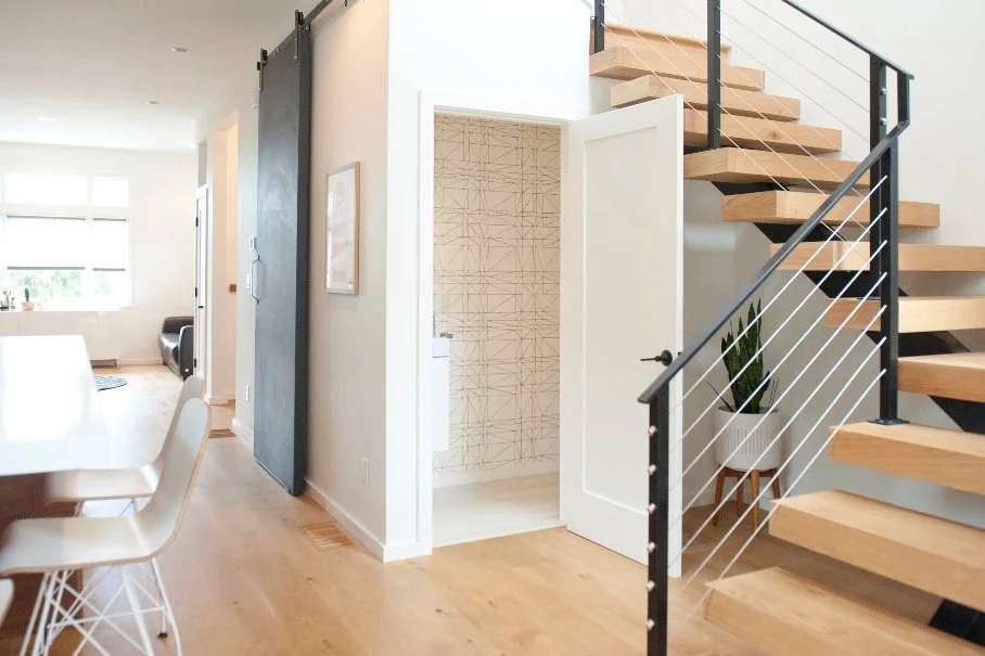 Interior view of a modern home with staircase, potted plant, and a small room with geometric wallpaper.