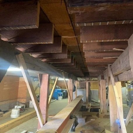 Underneath a wooden deck or platform, showing support beams and parts of the construction process.